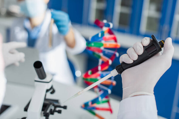 partial view of geneticist with micropipette near blurred microscope and dna model