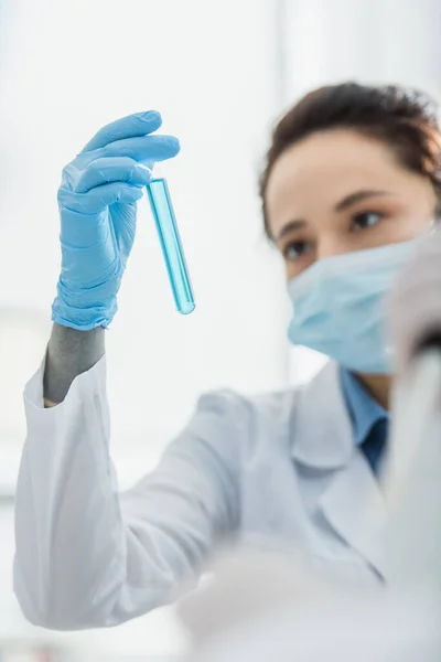 青い液体で検査管を見ている医療用マスクのぼやけた女性 — ストック写真