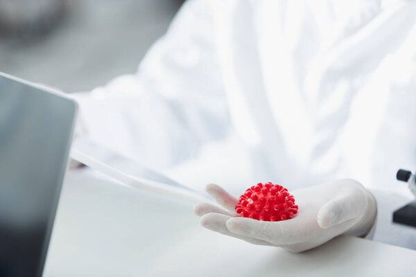 cropped view of virologist in latex glove holding red coronavirus bacteria in lab