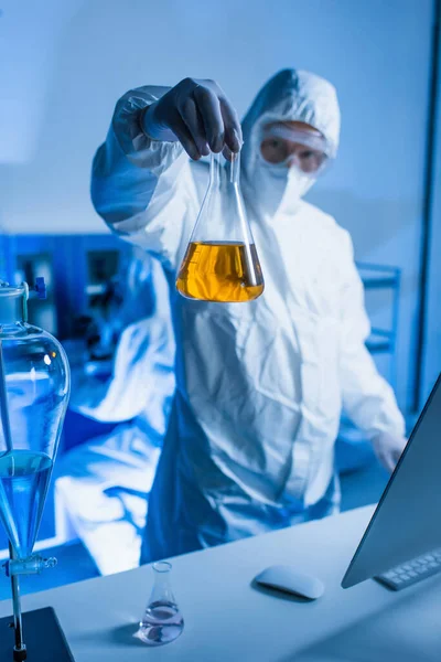 实验室里身穿危险物品套装拿着装有橙汁的瓶的模糊科学家 — 图库照片