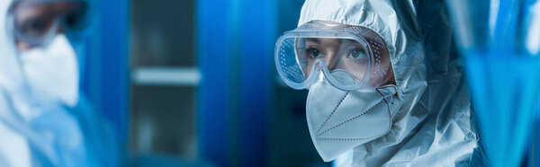 woman in goggles and medical mask near blurred scientist in laboratory, banner
