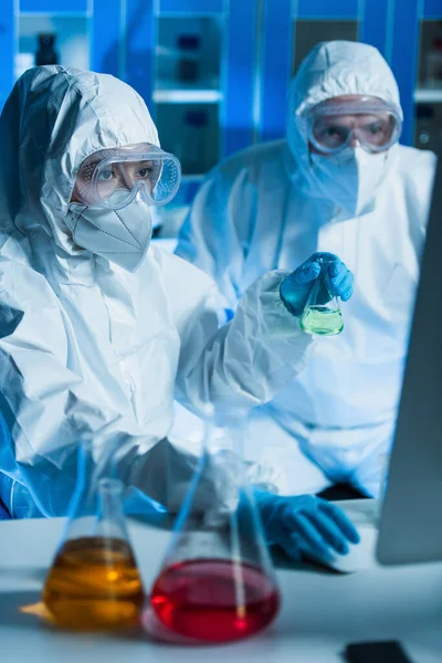 穿着防护服在实验室里工作的科学家们用五颜六色的液体在模糊的瓶中工作 — 图库照片