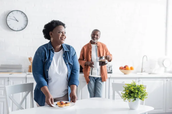 Happy Senior African American Woman Holding Plate Pancakes Blurred Husband — Stock Photo, Image