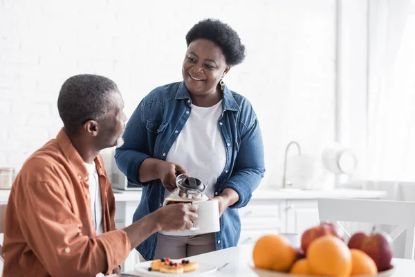 Χαρούμενη Αφροαμερικανή Σύζυγος Που Σερβίρει Καφέ Στον Χαμογελαστό Σύζυγο Κατά — Φωτογραφία Αρχείου