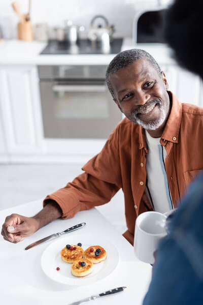happy african american man looking at wife holding cup during breakfast 