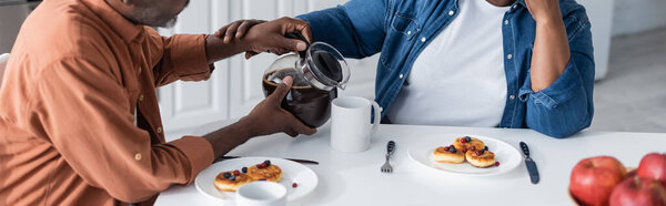 cropped view of senior african american man pouring coffee to wife during breakfast, banner