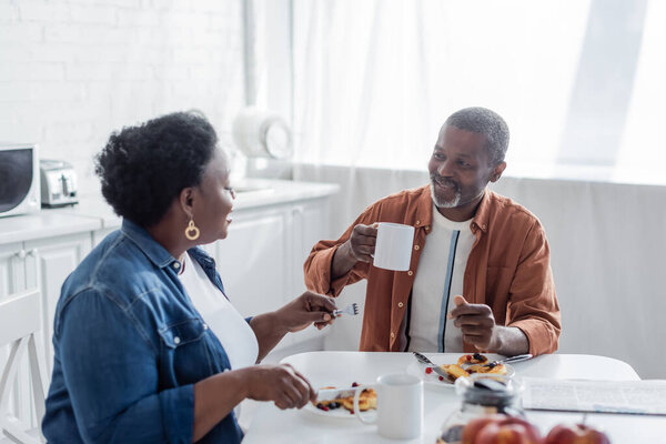 smiling african american man talking with senior wife during breakfast 