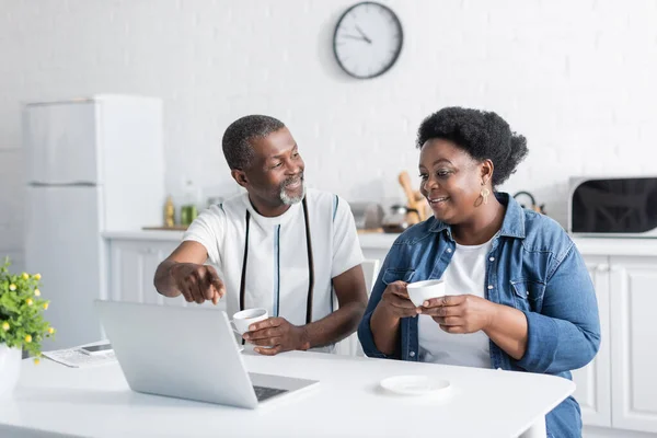 retired african american man pointing at laptop near wife