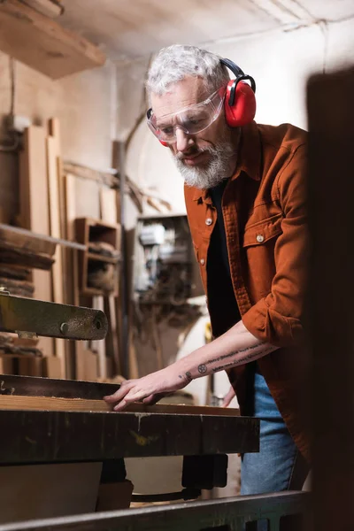 在模糊的前景下在工作台上工作的长胡子木匠 — 图库照片