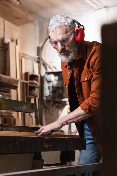 bearded carpenter working at workbench on blurred foreground
