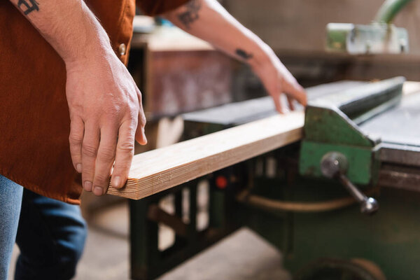 partial view of tattooed furniture designer with wooden plank in woodwork studio