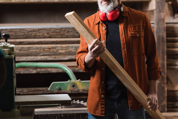 cropped view of bearded furniture designer holding wooden board in workshop