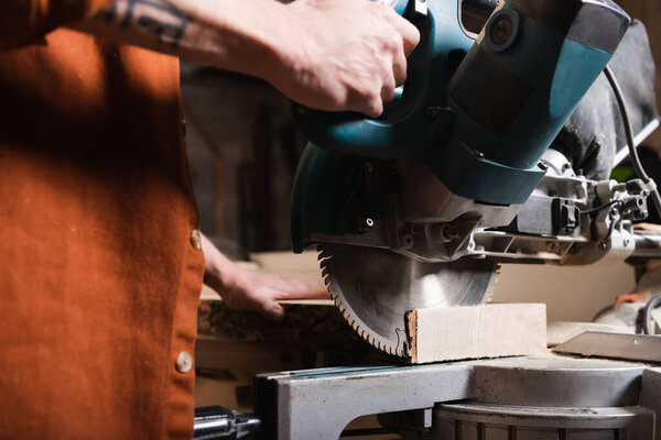 partial view of joiner cutting timber with miter saw