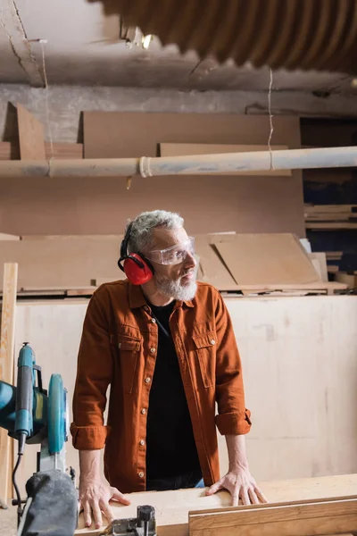 Woodworker Protective Earmuffs Goggles Looking Away Miter Saw — Stock Photo, Image