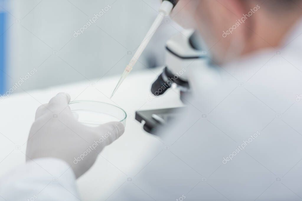 partial view of scientist with micropipette and petri dish in bio laboratory