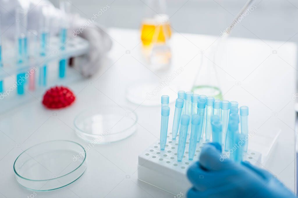 cropped view of scientists near test tubes and blurred petri dishes in laboratory