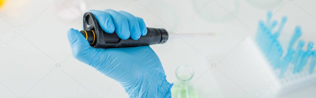 cropped view of scientist in blue latex glove using micropipette in lab, banner