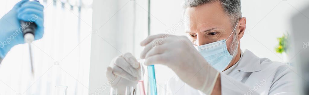 biotechnologist in medical mask and latex gloves working with test tubes in lab, banner