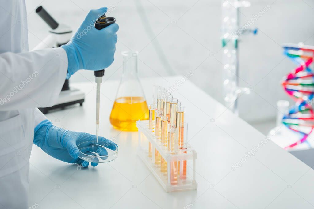 cropped view of geneticist with micropipette near flask and test tubes with yellow liquid