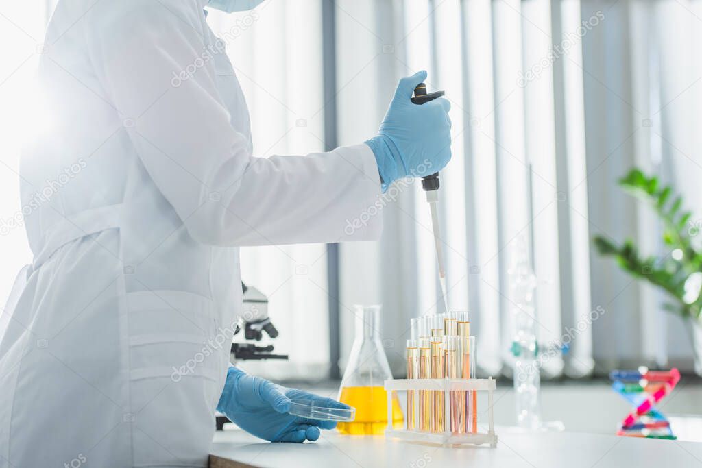 partial view of geneticist in white coat working with micropipette and test tubes
