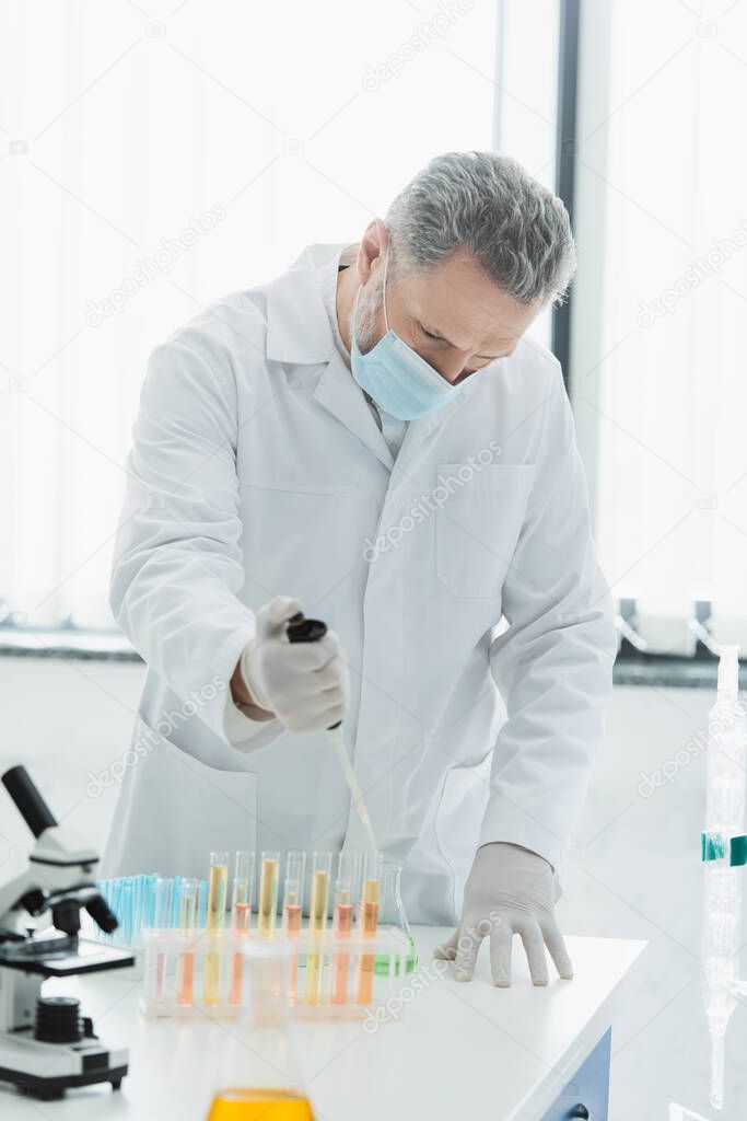 mature scientist in medical mask working with micropipette and test tubes