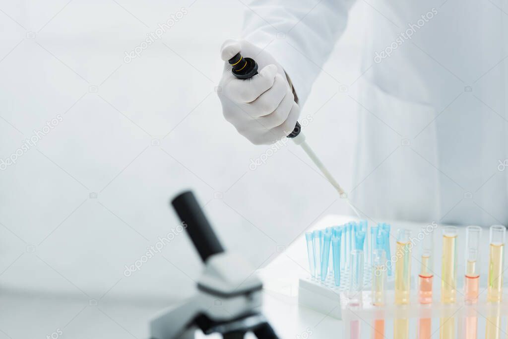 cropped view of bioengineer holding micropipette near test tubes with liquid