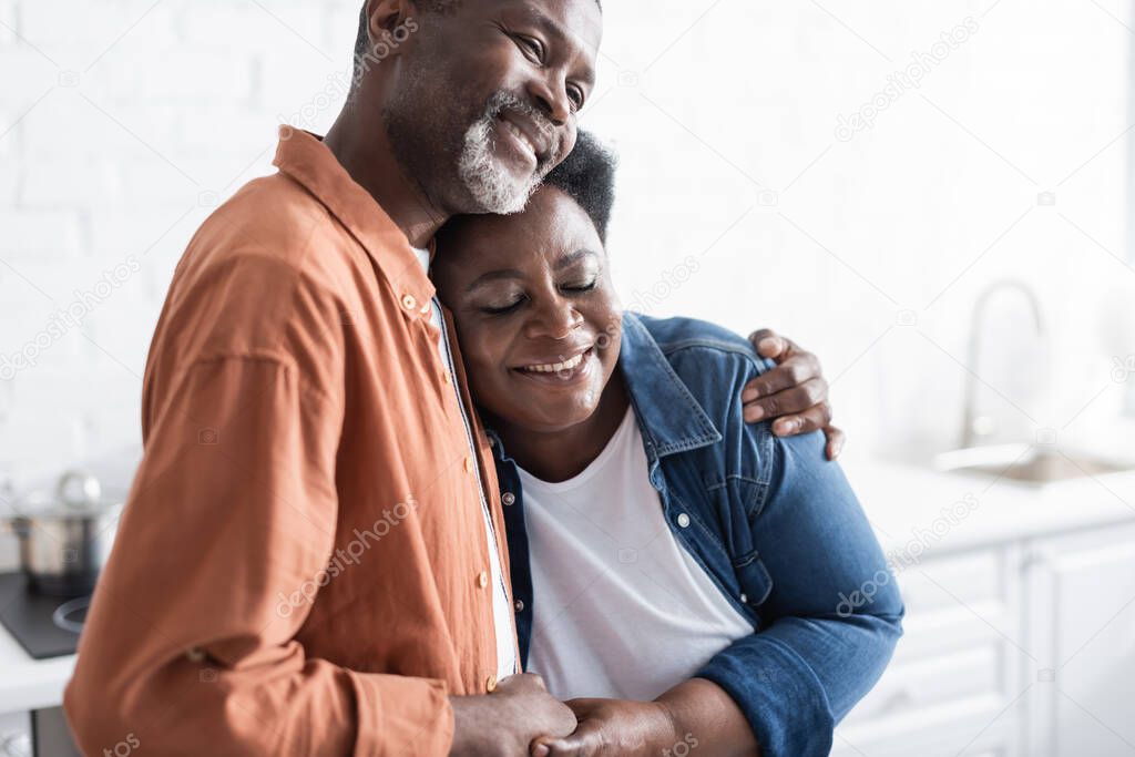 happy and senior african american couple holding hands and hugging at home