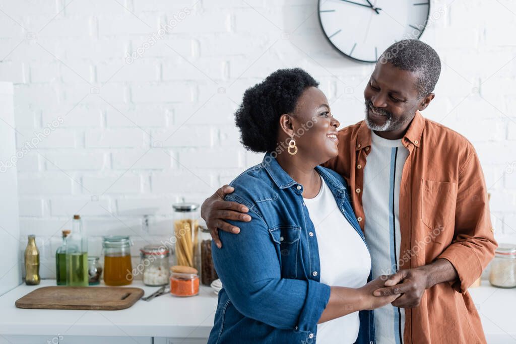 happy senior african american man looking at wife in kitchen