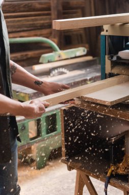 cropped view of tattooed carpenter working on bench thicknesser in workshop clipart