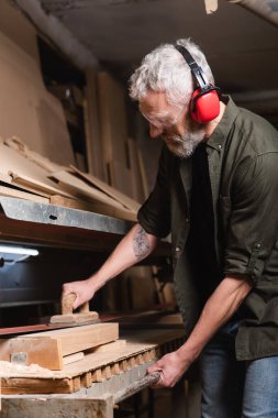 Yetişkin bir marangoz, zımpara makinesinde kulak kirletiyor.
