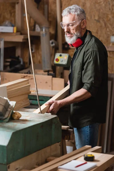 Stolarz Brodaty Trzymający Drewnianą Deskę Podczas Pracy Pracowni Stolarskiej — Zdjęcie stockowe