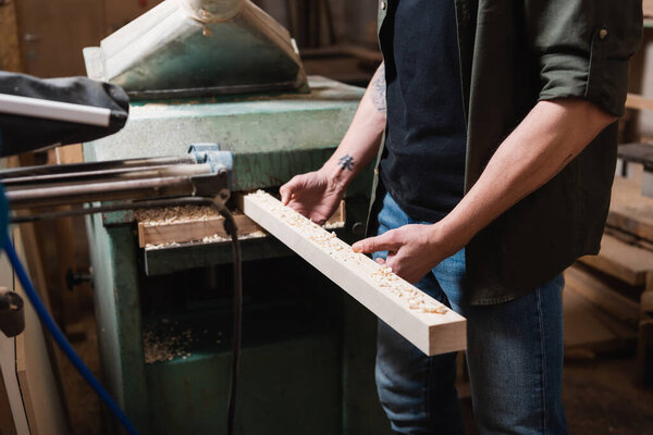 cropped view of furniture designer sawing wooden plank in thickness planner