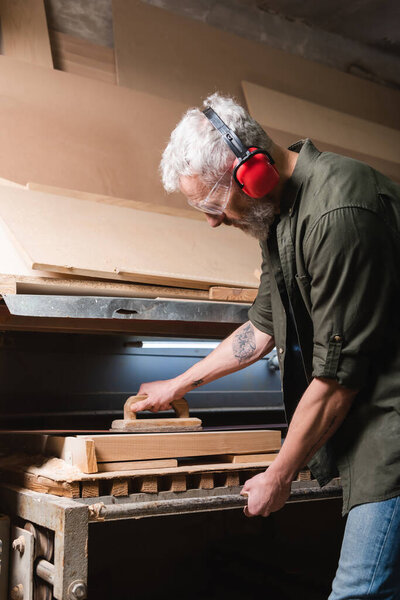 side view of grey haired carpenter polishing board in sander machine