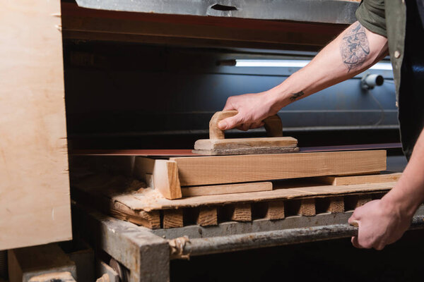 cropped view of tattooed carpenter polishing timber on sander machine