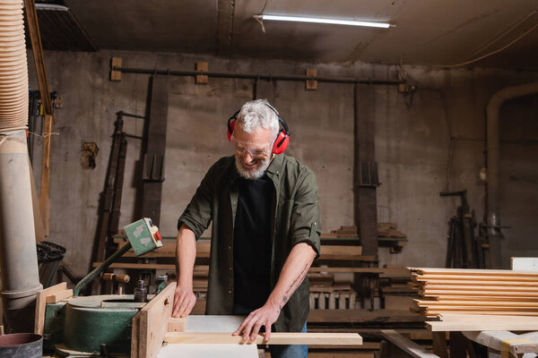 happy middle aged carpenter working on jointer machine in workshop
