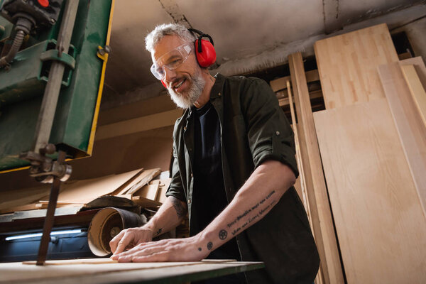 smiling carpenter cutting plywood on band saw in workshop