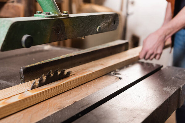 partial view of woodworker cutting plank on circular saw in carpentry workshop