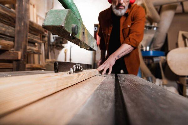 surface level on workbench with circular saw near cropped carpenter on blurred background