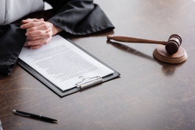 partial view of prosecutor with clenched hands near lawsuit and gavel on wooden desk clipart