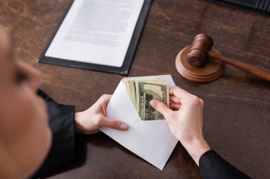 partial view of prosecutor with bribe in envelope near blurred gavel on desk clipart