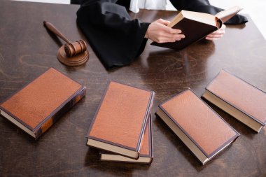 partial view of prosecutor reading book near collection of literature on desk clipart