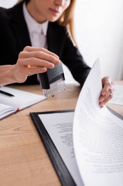 partial view of lawyer holding stamper near contract on blurred background clipart