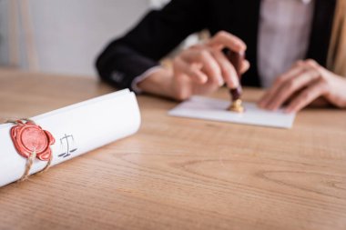 selective focus of rolled contract sealed with wax stamp near cropped notary on blurred background clipart