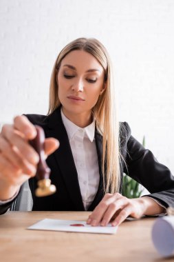 blonde notary holding blurred stamper near envelope on desk clipart