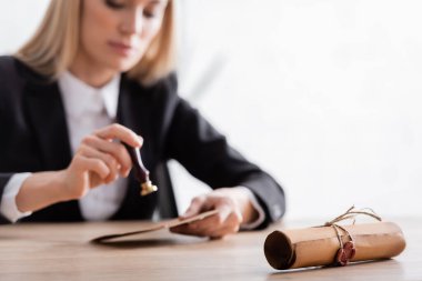 selective focus of rolled contract with wax seal near notary with stamper on blurred background clipart