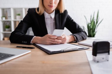 Pano yanında akıllı telefon kullanan noterin kısmi görünümü ve bulanık damga