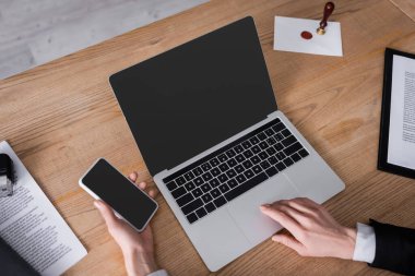 Avukatın cep telefonunu boş ekran ve belgelerle dizüstü bilgisayarın yanında tutarken kısmi görüntüsü