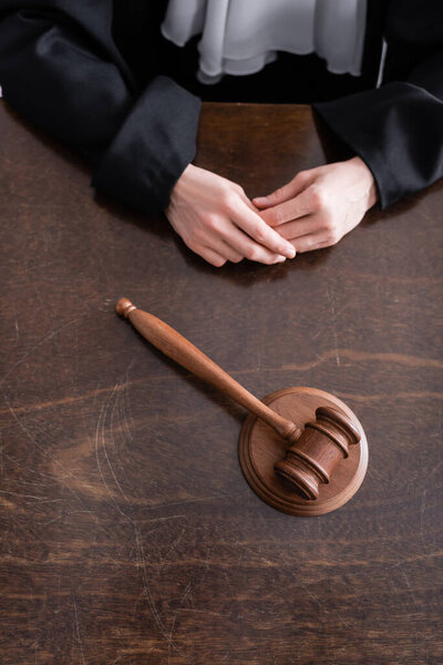 partial view of judge sitting near wooden gavel on desk