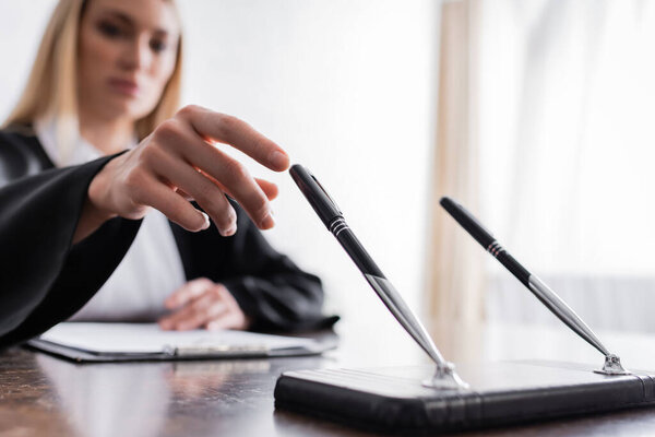 prosecutor reaching pen while sitting in office on blurred background