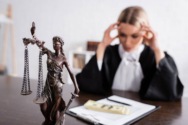 selective focus of themis statue near blurred prosecutor thinking near money and lawsuit